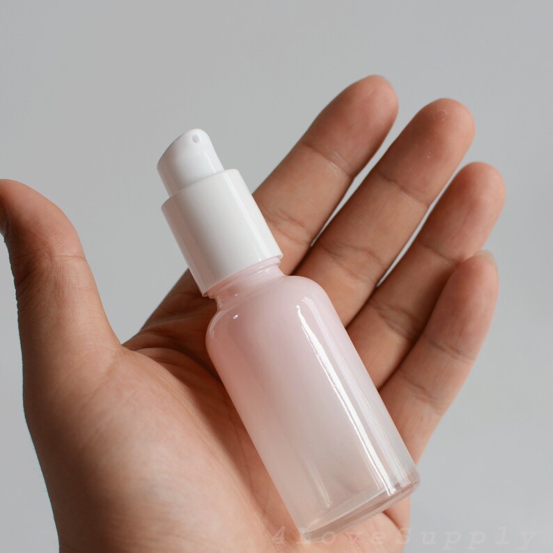 May include: A clear glass bottle with a white pump top. The bottle is filled with a light pink liquid.