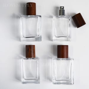 May include: Four rectangular clear glass perfume bottles with dark brown wooden caps. Three bottles are capped, while one bottle is shown with its wooden cap removed, revealing a silver spray nozzle. The text 4LOVESUPPLY is visible in the image.