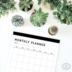 May include: A black and white monthly planner with the text "MONTHLY PLANNER" at the top. The planner has a grid layout with days of the week labeled: Sun, Mon, Tue, Wed, Thu, Fri, Sat. The planner is on a white background with small potted plants around it.