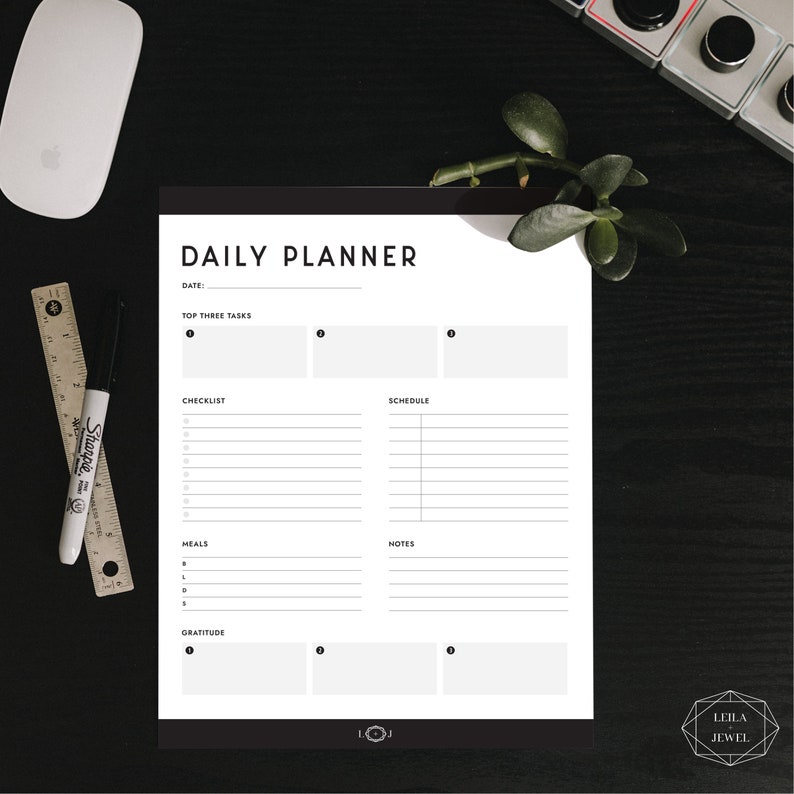 May include: A black and white daily planner with sections for top three tasks, checklist, schedule, meals, notes, and gratitude. The planner has a simple design with a black header and white text.