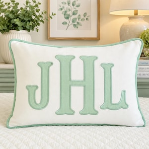 May include: A rectangular white throw pillow featuring a large, centred, embroidered monogram with the letters JHL in a soft sage green colour. The pillow is finished with matching sage green piping along all four edges of the rectangular cover.