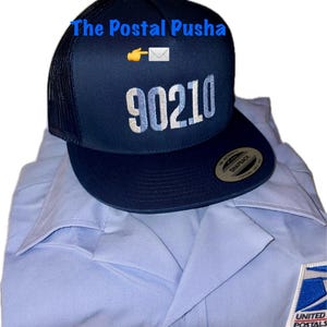 May include: A navy blue trucker hat with the text "The Postal Pusha" and "90210" embroidered in white. The hat is placed on top of a light blue postal uniform shirt with a United States Postal Service patch.