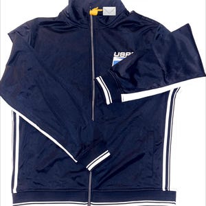May include: Navy blue zip-up track jacket with white stripes down the sleeves and sides. The jacket has a stand-up collar, a small logo on the chest, and the text "The Postal Pusha" at the top.
