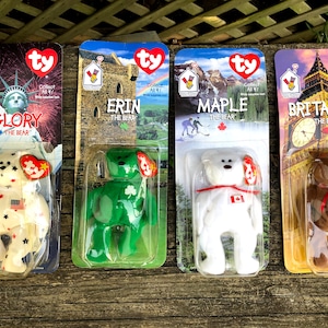 May include: Four Ty Beanie Babies in their original packaging. The bears are named Glory, Erin, Maple, and Britannia. Each bear is wearing a different outfit representing a different country. The bears are all white with different colored outfits. The packaging is colorful and features images of landmarks from each country.