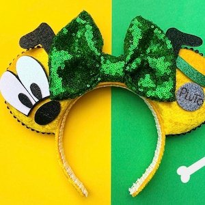 May include: Yellow and green Minnie Mouse ears with a Pluto character design. The ears are covered in plush fabric and feature a green sequin bow. The right ear has a silver charm with the word "Pluto" on it.