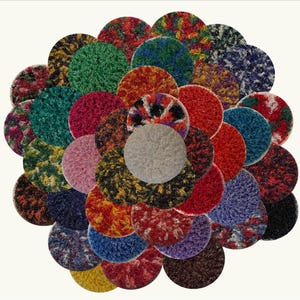 Puede incluir: Surtido de discos de lija redondos y texturizados de varios colores. Los discos están dispuestos en un patrón circular, que se asemeja a una flor.