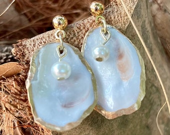 May include: A pair of white pearl earrings with a gold setting. The earrings are shaped like an oyster shell.