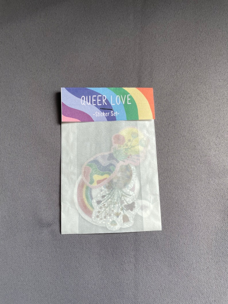 May include: A sticker set in a clear plastic package. The packaging has a rainbow design with the words "QUEER LOVE" and "-Sticker Set-". The stickers inside feature rainbow designs and floral elements.