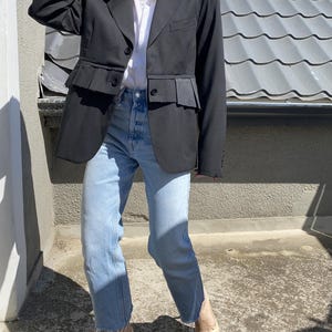 Puede incluir: Una chaqueta negra con un dobladillo con volantes, usada con jeans azul claro y tacones crema.