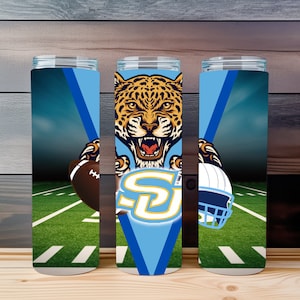 May include: Three tall, cylindrical tumblers with a football theme. Each tumbler features a different design element: a football, a jaguar, and a football helmet. The background depicts a football field and a blue sky.