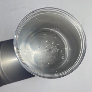 May include: A clear plastic container with a white liquid inside. The liquid has small bubbles throughout.