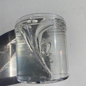 May include: A clear plastic container filled with a clear, viscous liquid that is swirling in a vortex pattern.