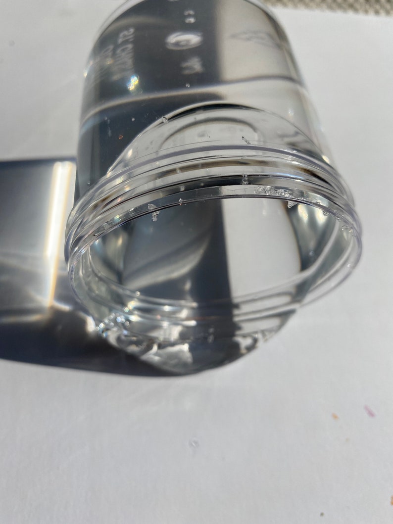 May include: A clear plastic container with a textured surface. The container is filled with a clear liquid.