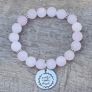 May include: A pink rose quartz beaded bracelet with a silver charm that reads "grateful thankful blessed".