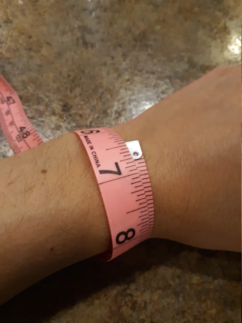 May include: Pink measuring tape wrapped around a wrist, showing a measurement of 7 inches. The tape reads "Made in China".