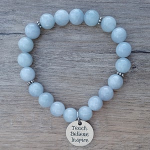 May include: A light blue aquamarine gemstone bracelet with silver beads and a silver charm that reads "Teach Believe Inspire".