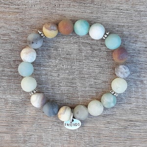 May include: A beaded bracelet with a mix of green, brown, and white stones. The bracelet has a silver charm that says "FRIENDS".