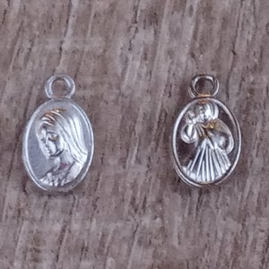 May include: Two silver oval charms, one with a depiction of the Virgin Mary and the other with a depiction of a woman holding a baby.