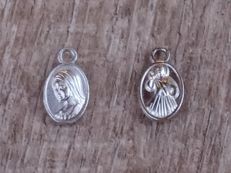 May include: Two silver oval charms, one with a depiction of the Virgin Mary and the other with a depiction of a woman holding a baby.