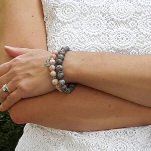 Puede incluir: Dos pulseras apiladas en la mu&ntilde;eca de una persona. La pulsera superior est&aacute; hecha de piedras de color rosa claro y gris. La pulsera inferior est&aacute; hecha de piedras de color gris oscuro. Ambas pulseras tienen detalles plateados.