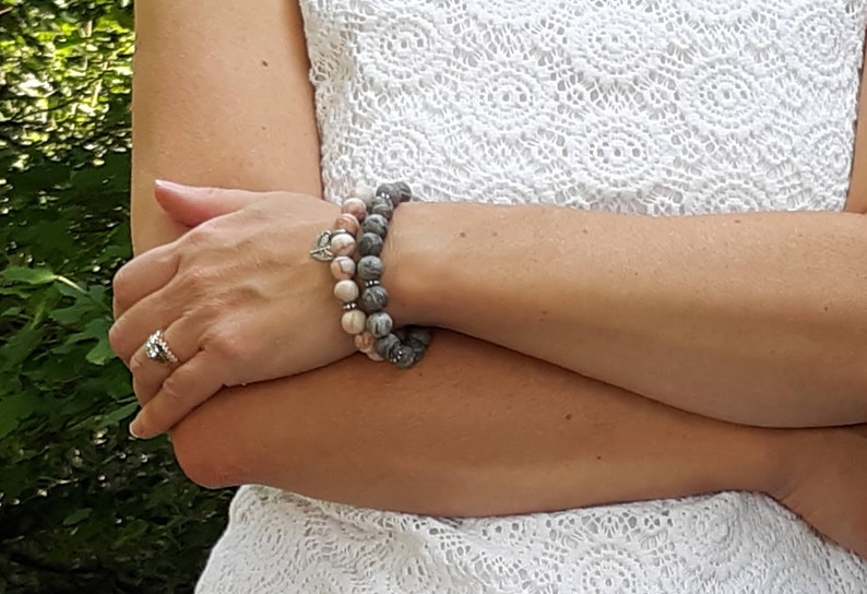 Puede incluir: Dos pulseras apiladas en la mu&ntilde;eca de una persona. La pulsera superior est&aacute; hecha de piedras de color rosa claro y gris. La pulsera inferior est&aacute; hecha de piedras de color gris oscuro. Ambas pulseras tienen detalles plateados.