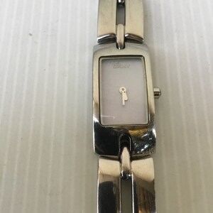 Op de afbeelding: Een zilveren horloge met een witte wijzerplaat en een zilveren band. De wijzerplaat van het horloge heeft een sleutel-vormige wijzer en het woord "DKNY" erop gedrukt.
