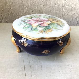 Peut inclure: Une boîte à bijoux en porcelaine bleue et blanche avec des accents dorés et un motif floral sur le couvercle. La boîte a trois pieds dorés.