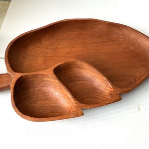 Peut inclure: Un grand plateau de service en bois en forme de feuille avec trois compartiments. Le plateau est en bois brun rougeâtre chaud et a une finition lisse et polie. La conception de la feuille comprend une poignée. Ce plateau est idéal pour servir des collations ou des apéritifs.