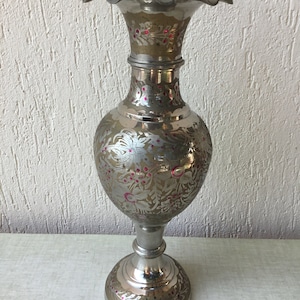 Pode incluir: Um vaso de prata com uma borda festonada e desenhos florais intrincados em prata e rosa. O vaso tem um corpo redondo e uma base alargada.