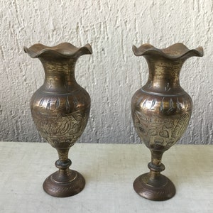 Könnte beinhalten: Zwei verzierte Messingvasen mit aufwendigen floralen Mustern. Die Vasen haben einen gewellten Rand und einen ausgestellten Fuß.