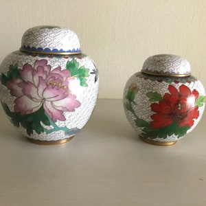 Peut inclure: Deux pots en porcelaine cloisonnée avec des motifs floraux. Le plus grand pot a une fleur rose et le plus petit pot a une fleur rouge.