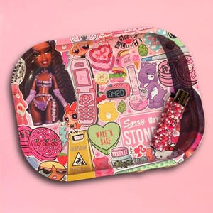 May include: Pink rolling tray with a collage of cartoon characters, a doll, and the text "Baked Babe" and "Sorry We're Stoned". The tray also features a bedazzled vape pen and a caution sign.