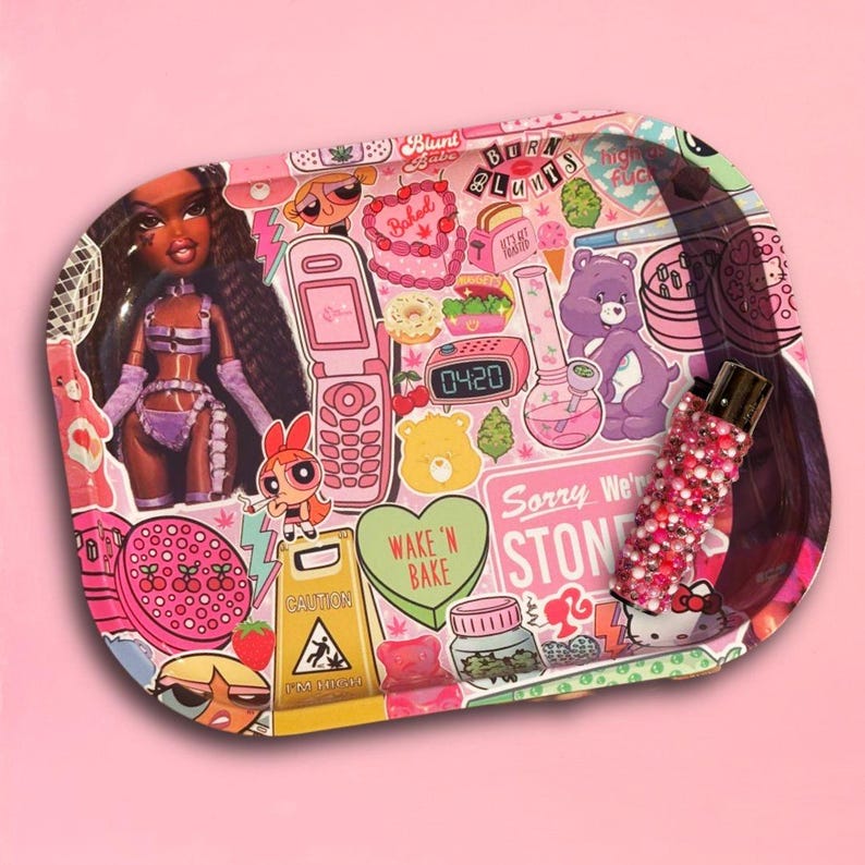 May include: Pink rolling tray with a collage of cartoon characters, a doll, and the text "Baked Babe" and "Sorry We're Stoned". The tray also features a bedazzled vape pen and a caution sign.