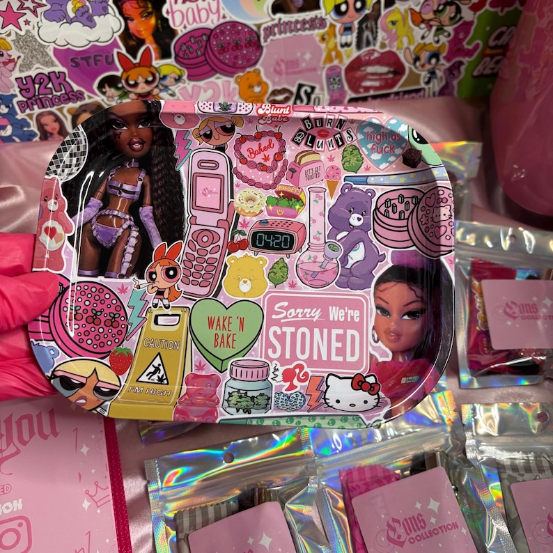 May include: A pink rolling tray with a collage of stickers and a doll. The tray features images of a flip phone, a bong, a Care Bear, and the text "Sorry We're Stoned." Other stickers include "Baked" and "Wake 'N Bake."