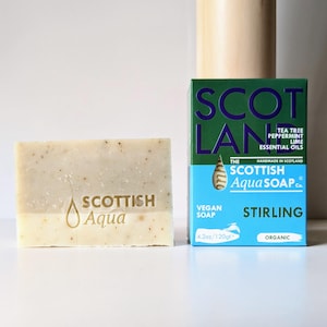 Può includere: Una saponetta Scottish Aqua e la sua scatola. Il sapone è beige chiaro con macchie. La scatola è verde e blu e riporta "Tea Tree Peppermint Lime Essential Oils" e "Stirling". Il sapone pesa 120g.