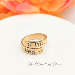 May include: Gold-toned adjustable ring with the words "BE STILL" engraved on the band. A small floral design is engraved on the opposite side of the band.