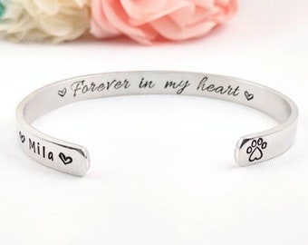 May include: Silver bracelet with the inscription "Forever in my heart" and a paw print charm. The bracelet also has the name "Mila" engraved on it.