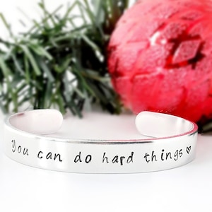 May include: Silver bracelet with the inscription "you can do hard things" and a small heart symbol.