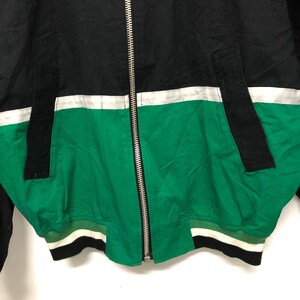 May include: A black, white, and green bomber jacket with a zipper closure. The jacket has a white stripe across the chest and a green bottom with a white and black stripe.