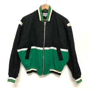 May include: A black and green bomber jacket with a zipper closure. The jacket has white stripes on the sleeves and a white stripe across the chest. The jacket has a green and white striped collar.