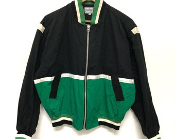Può includere: Una giacca bomber nera e verde con chiusura a zip. La giacca ha delle strisce bianche sulle maniche e una striscia bianca sul petto. La giacca ha un colletto a righe verdi e bianche.