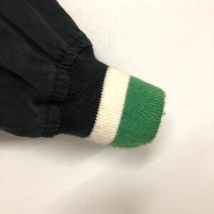 May include: Black bomber jacket with a green, white, and black striped cuff.