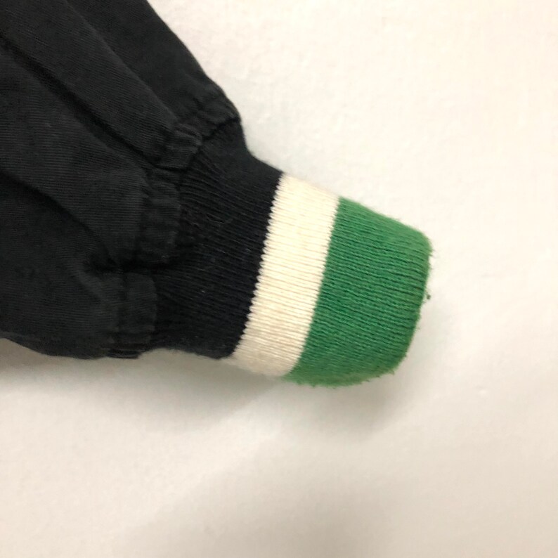 May include: Black bomber jacket with a green, white, and black striped cuff.