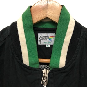 May include: Black bomber jacket with a green and white striped collar. The jacket has a zipper closure and a Benetton Formula 1 Racing Team label with the text "Trade Mark" and the number "46".