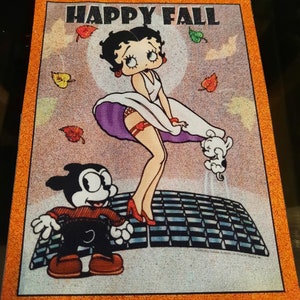 Peut inclure: Un patch de style vintage représentant une image de dessin animé de Betty Boop dans une robe blanche avec une jupe violette, des chaussures rouges et une jarretière rouge. Elle se tient sur une plateforme à carreaux avec un chien de dessin animé noir et blanc à côté d'elle. Le texte "HAPPY FALL" est imprimé en orange en haut du patch.