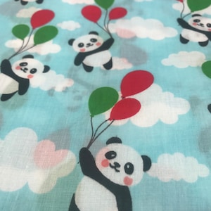 May include: A blue fabric with a repeating pattern of white pandas holding red and green balloons. The pandas are flying in a blue sky with white clouds.