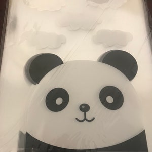 May include: A stack of clear plastic bags with a black and white panda face design printed on the front. The panda has large black eyes, a small black nose, and a black mouth.