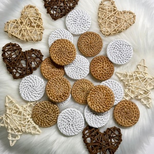 May include: A collection of round woven rattan coasters in white and natural brown colors. The coasters are arranged on a white fluffy surface with decorative woven hearts and stars.