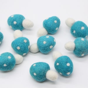 Puede incluir: Diez setas de fieltro de color azul turquesa con lunares blancos. Cada seta tiene un tallo de fieltro blanco.