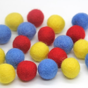 Könnte beinhalten: Eine Sammlung von Filzkugeln in den Farben Rot, Gelb und Blau. Die Kugeln sind in einem zufälligen Muster angeordnet.